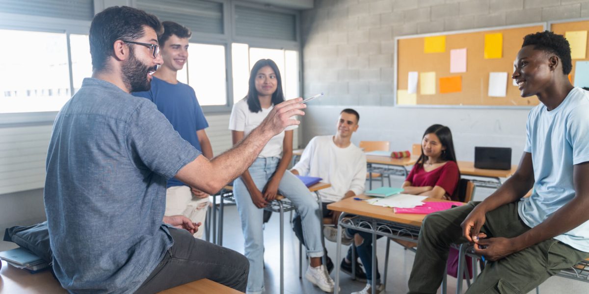 Group of teenager students with young teacher at classroom, sitting talking and sharing conversation together