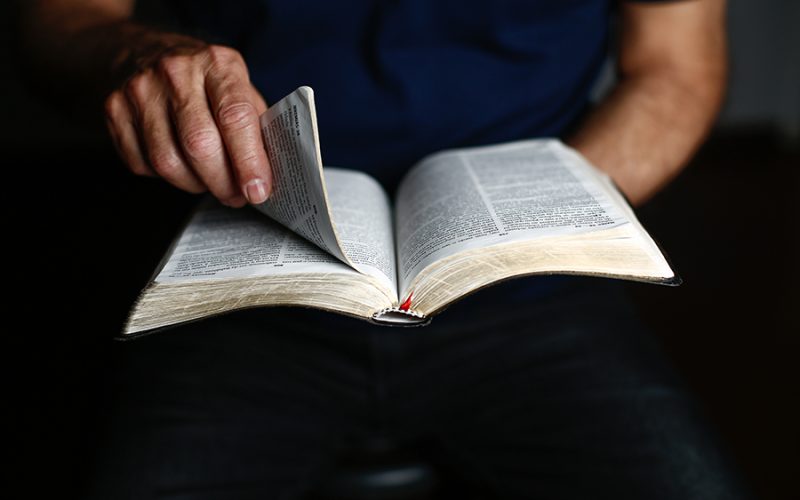 Egy férfi a kezével nyitja ki a Bibliát