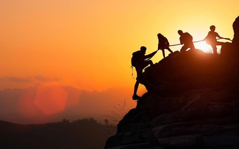 Silhouette of the climbing team helping each other while climbing up in a sunset. The concept of aid.