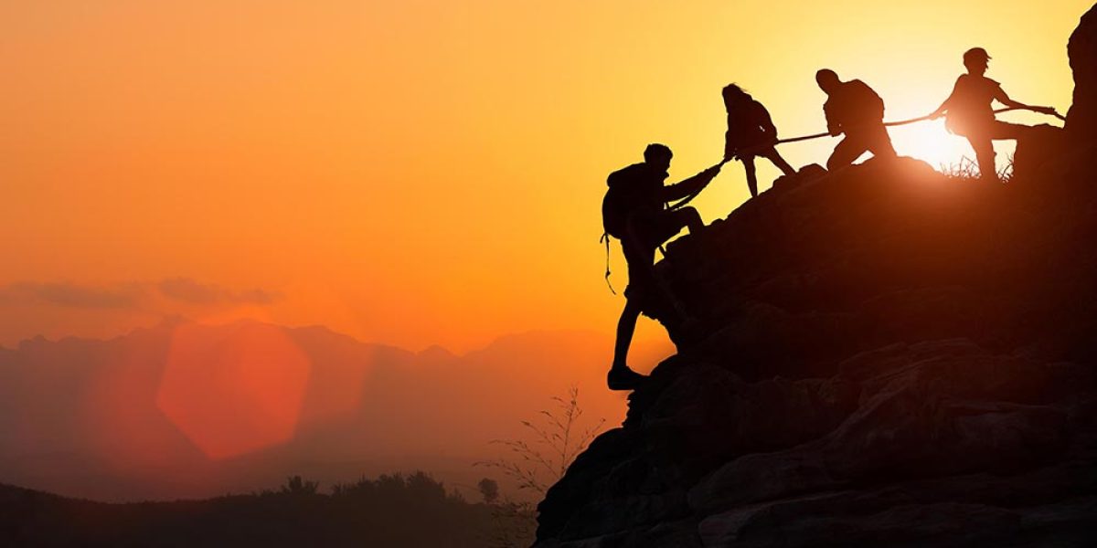 Silhouette of the climbing team helping each other while climbing up in a sunset. The concept of aid.